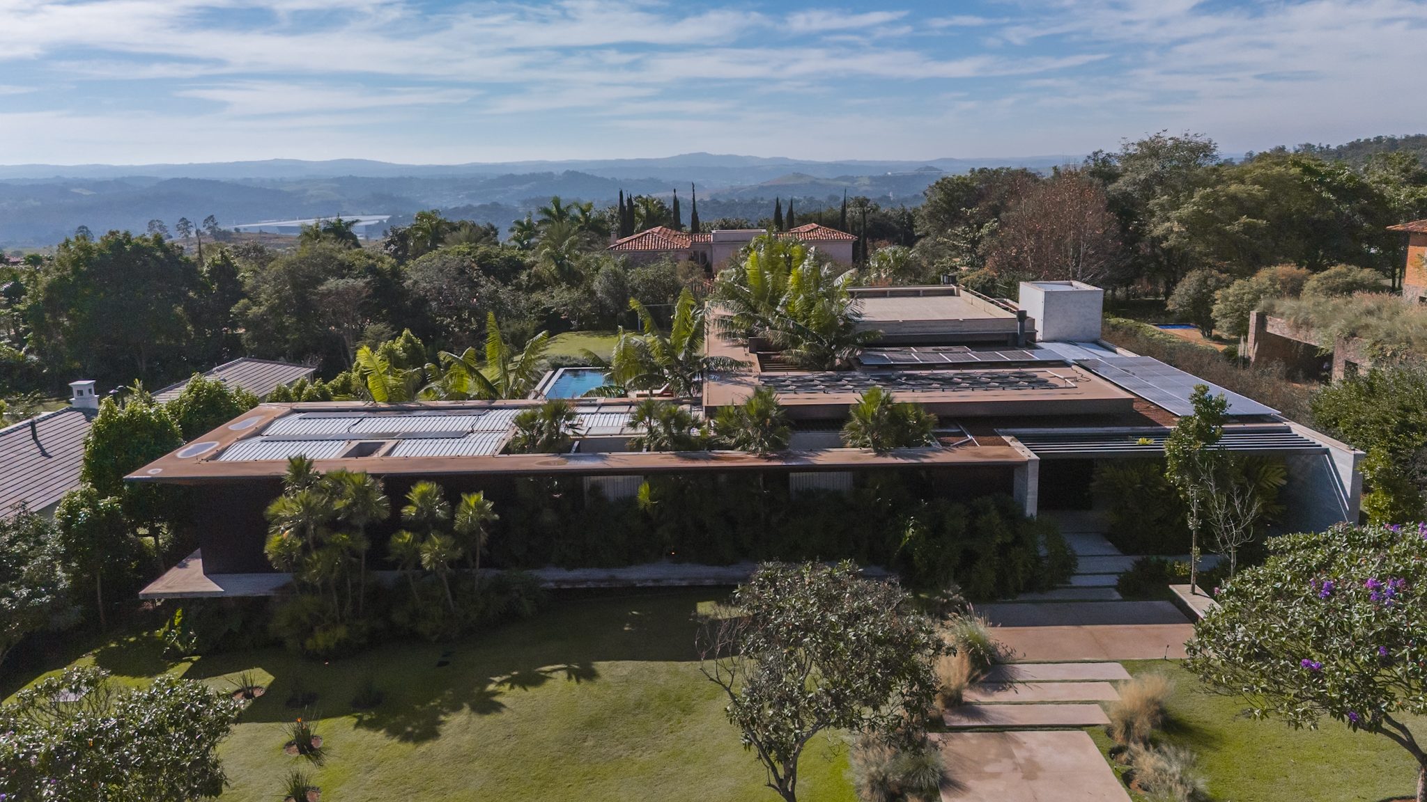 Vista aérea da casa entre palmeiras, com o horizonte da Fazenda da Grama ao fundo