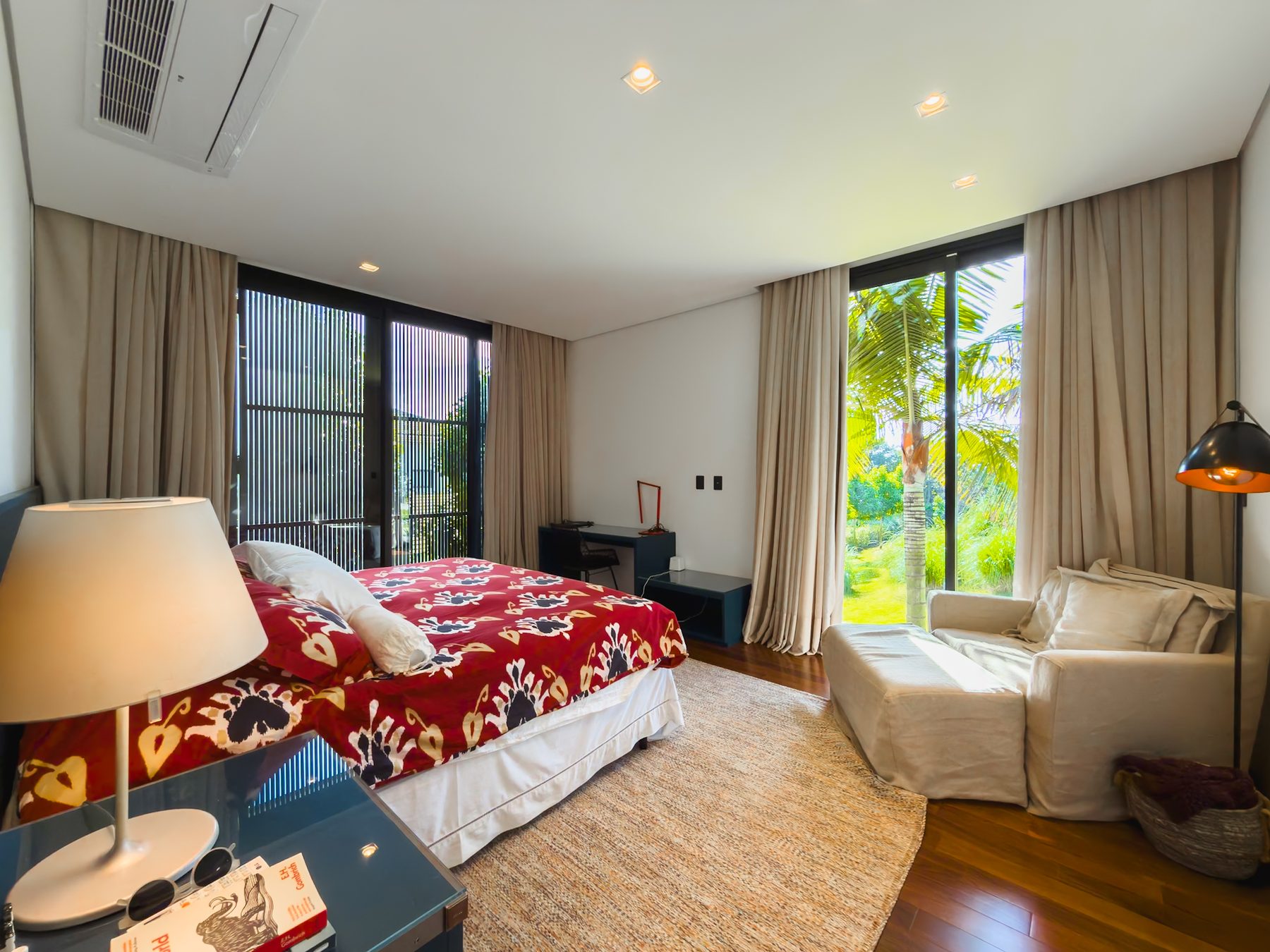 Suíte principal com cama de casal, colcha estampada e porta de vidro aberta para o jardim