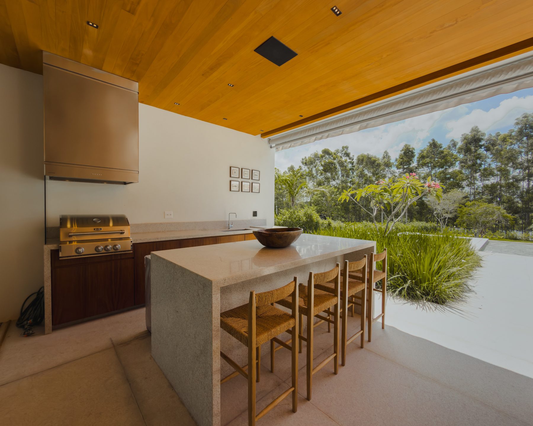 Espaço gourmet com bancada de pedra, banquetas de madeira e vista para o jardim