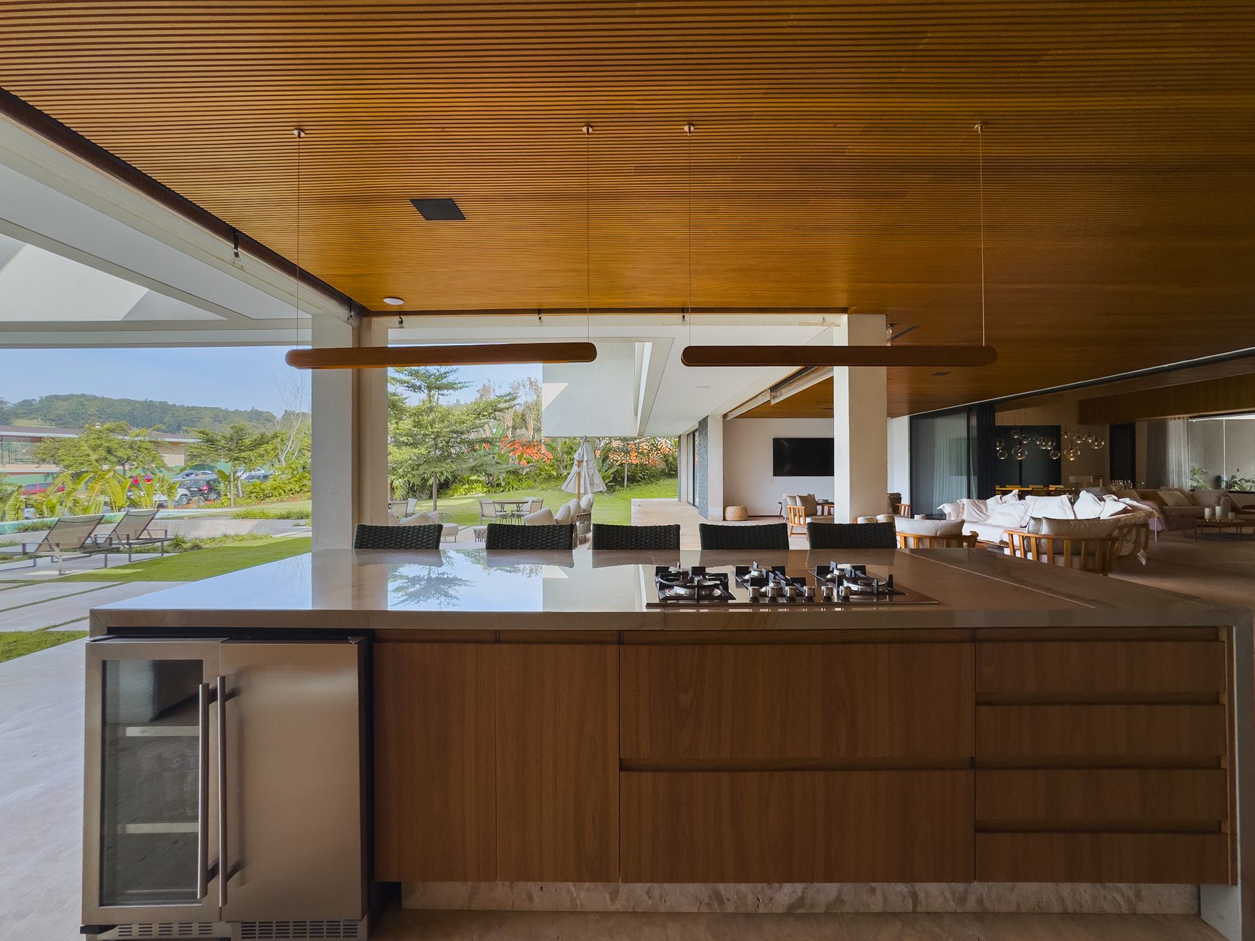 Espaço gourmet com ilha de madeira e cooktop, aberto para o jardim e a piscina