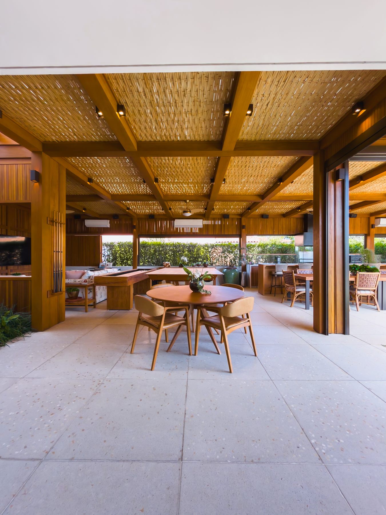 Mesa redonda com cadeiras de madeira sob o pergolado, aberto para o gramado