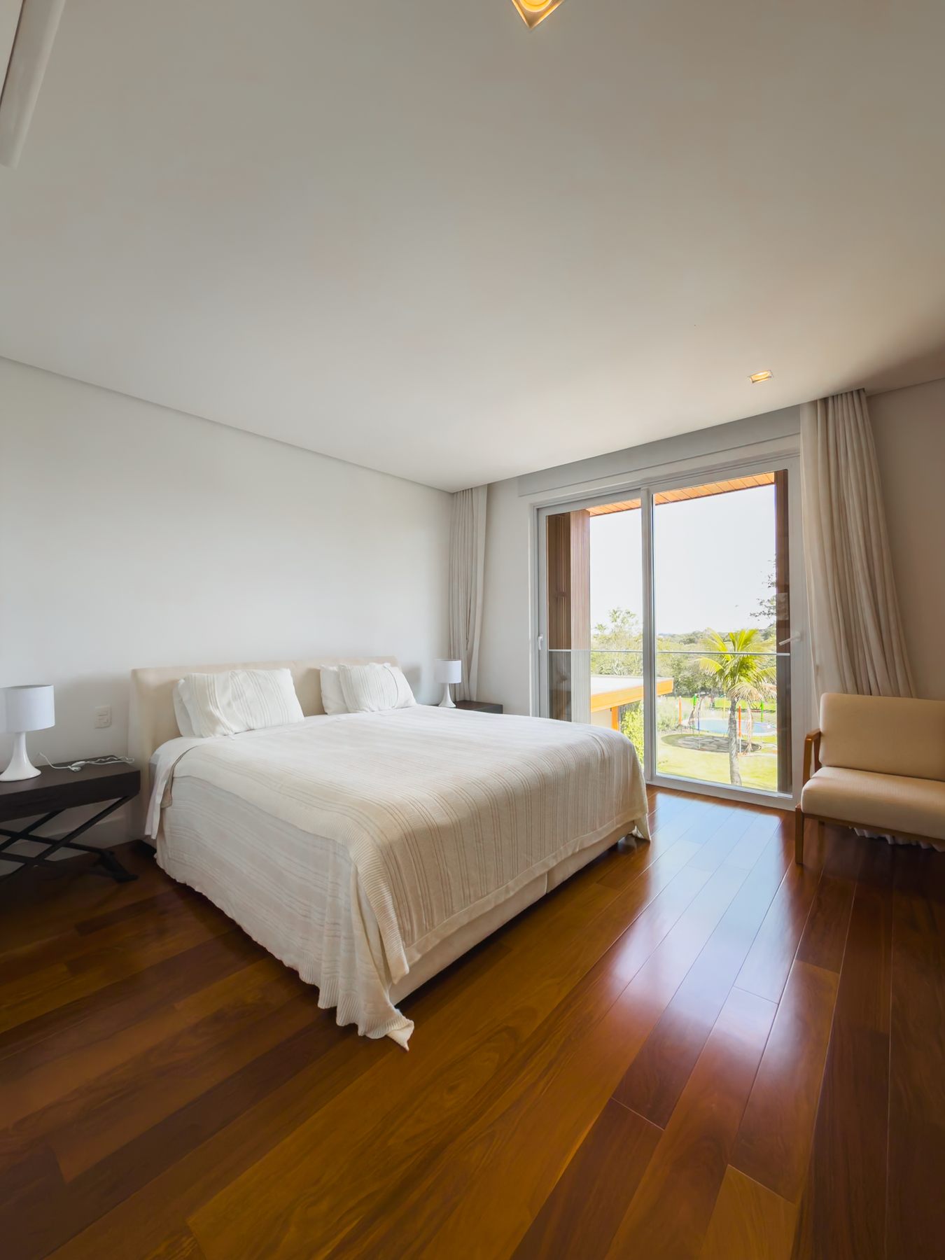 Suíte com cama de casal, piso de madeira e porta de vidro para a varanda