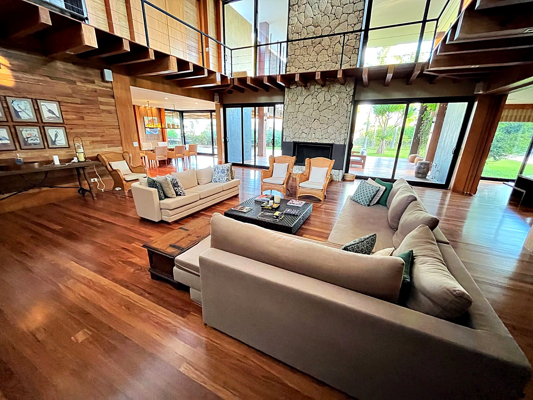 Living de pé-direito duplo com sofás, mezanino de madeira e a coluna de pedra da lareira