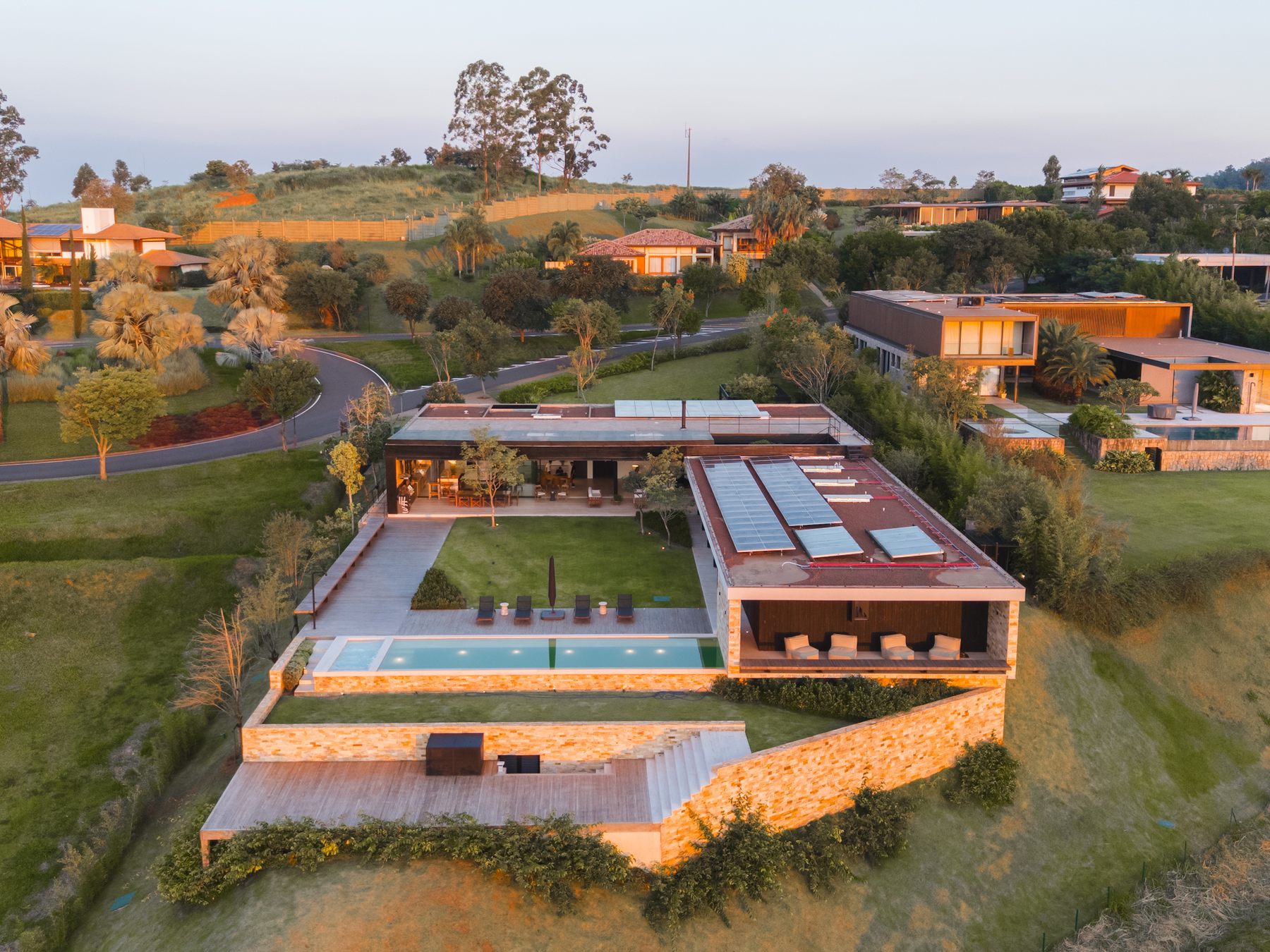 Vista aérea da casa em torno do jardim central, com a piscina, o deck e o talude de pedra voltados ao campo