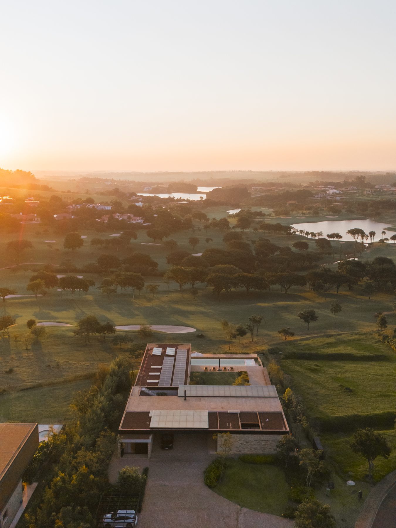 A casa vista do alto ao amanhecer, com o campo de golfe e os lagos até o horizonte