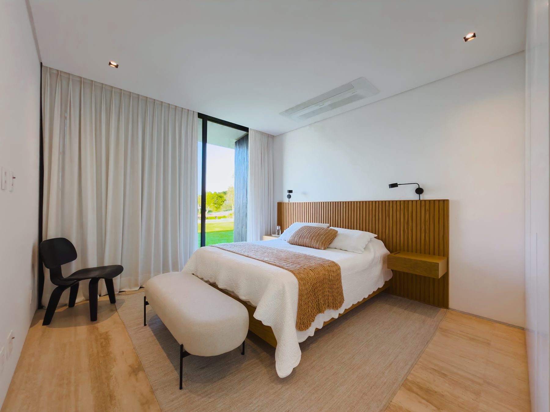 Suíte com cama de casal, cabeceira de madeira e janela de vidro para o gramado